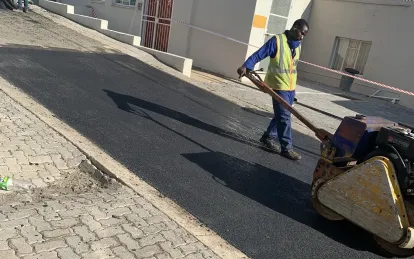 A walk-behind roller compacting a freshly laid strip of hot asphalt alongside brick paving.