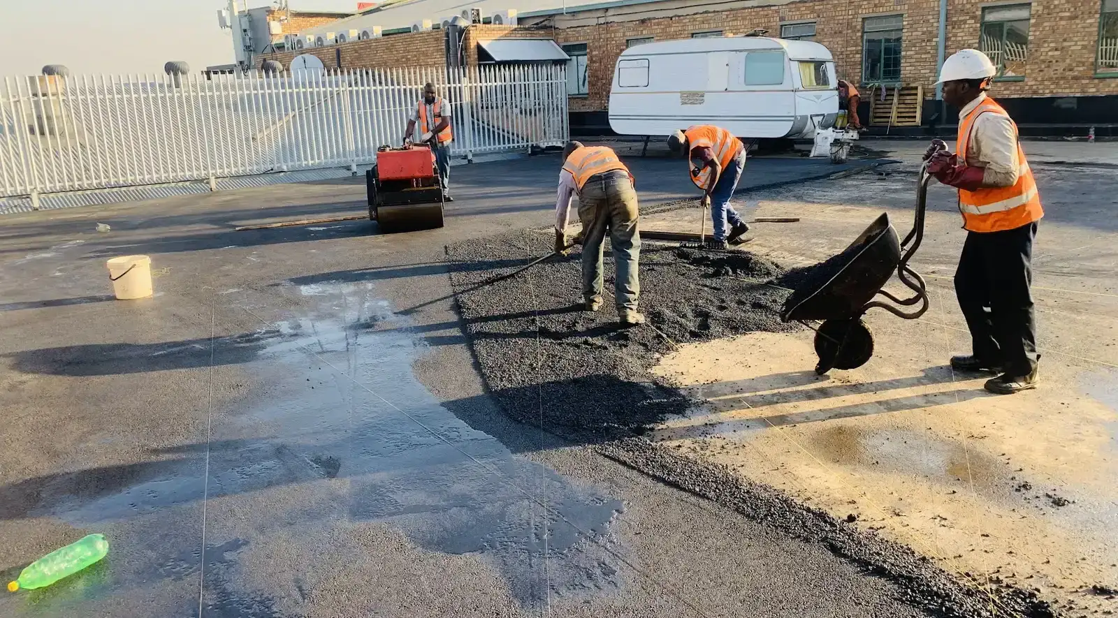 A Tar Surfacing crew raking and rolling hot asphalt across a commercial yard at first light.