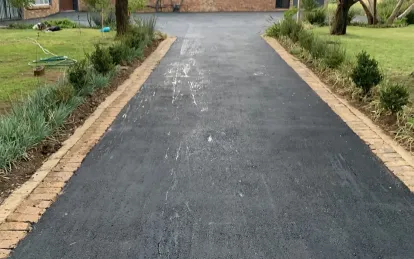 A finished tarred driveway with brick kerbing, running between planted garden beds.